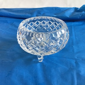May include: A clear glass bowl with a diamond pattern and three legs. The bowl is on a blue background.