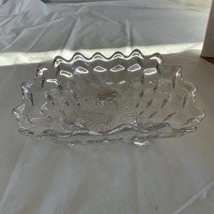 May include: A clear glass serving bowl with a scalloped edge and a textured, diamond-shaped pattern. The bowl has a wide, shallow base and is designed for serving fruit, snacks, or other small items.