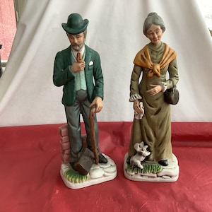 Pair Elderly Man/Woman Bisque Figurines - Woman w/Dog At Her Feet-Hankie in Hand-Bag on Her Arm-Shawl Around Her Shoulders -See Desc