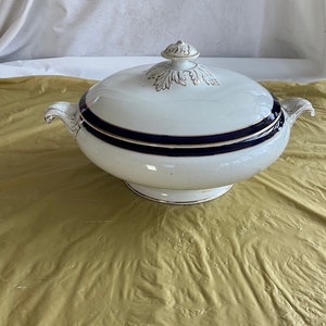 May include: White porcelain serving bowl with a blue and gold trim. The bowl has a lid with a decorative gold design.