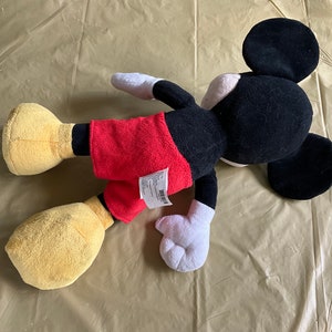 May include: A black and red plush Mickey Mouse toy with yellow shoes and a white tag on the back.