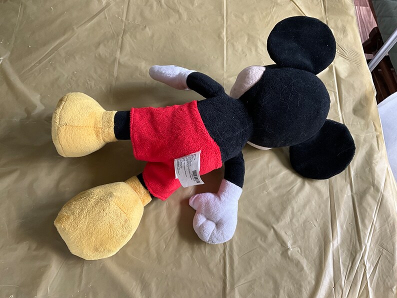 May include: A black and red plush Mickey Mouse toy with yellow shoes and a white tag on the back.