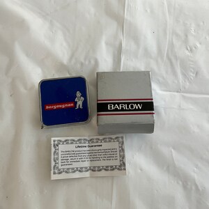 May include: A blue and silver tape measure with the word "bergougnan" printed on it. The tape measure is in a silver box with the word "BARLOW" printed on it. The box also includes a small card with the text "Lifetime Guarantee".