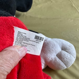 May include: A red and black plush Mickey Mouse toy with a white tag that reads "Made in China &copy;Disney Hand Wash Only REG NO PAF13942(CN) 00016745 ALL NEW MATERIALS-POLYESTER FIBERS AND POLYESTER FELT POR 955036 Manufacturer: Feld Consumer Products 800 Feld Way Palmetto FL 34221 USA Hands"