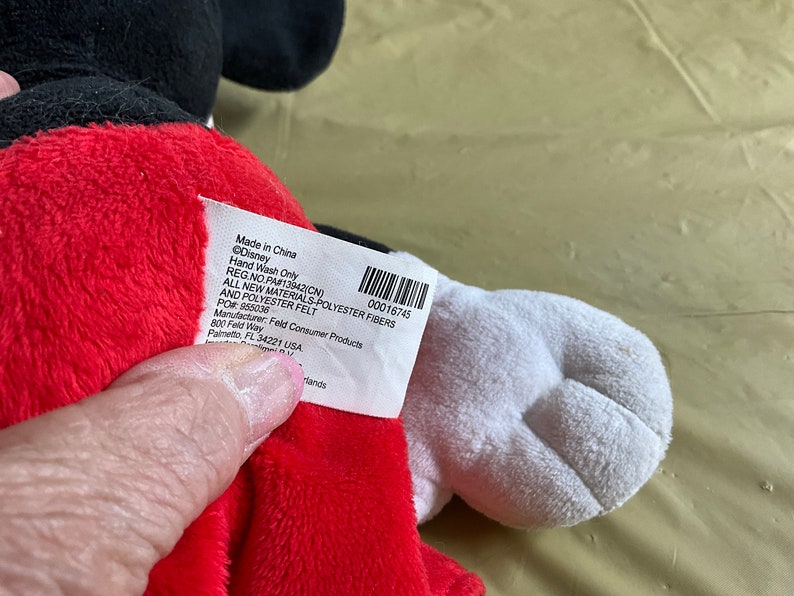 May include: A red and black plush Mickey Mouse toy with a white tag that reads "Made in China &copy;Disney Hand Wash Only REG NO PAF13942(CN) 00016745 ALL NEW MATERIALS-POLYESTER FIBERS AND POLYESTER FELT POR 955036 Manufacturer: Feld Consumer Products 800 Feld Way Palmetto FL 34221 USA Hands"