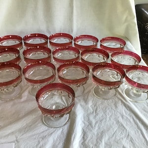 May include: A set of 13 clear glass dessert dishes with a red rim. The dishes have a scalloped edge and a pedestal base.