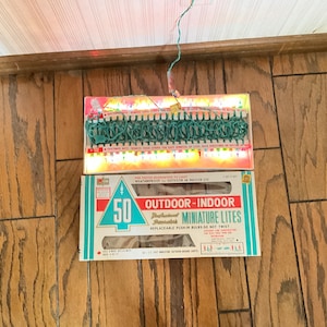 May include: A box of 50 outdoor-indoor miniature lights with a green wire and clear bulbs. The box is white with blue and red accents and says "50 Outdoor-Indoor Miniature Lights" and "Weatherproof for Outdoor or Indoor Use".