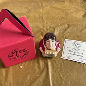 May include: A red box with a handle and the text "FACE KEVIN FRANCIS POTTS 2000" on the front. A ceramic figurine of a person holding a loaf of bread. A certificate of authenticity with the text "FACE KEVIN FRANCIS POTTS 2000 Certificate of Authenticity" on it.