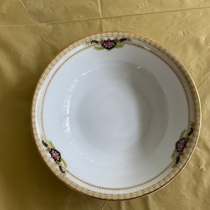May include: A white ceramic bowl with a gold and brown rim and floral designs. The bowl has a white interior and a slightly raised rim.