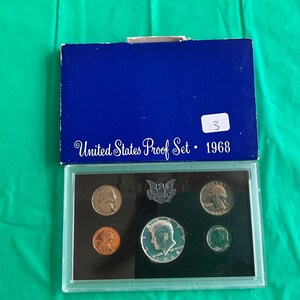 May include: A 1968 United States Proof Set in a blue box. The set includes various coins, such as a penny, nickel, dime, quarter, and half dollar, displayed in a clear plastic case. The box has the text "United States Proof Set 1968".