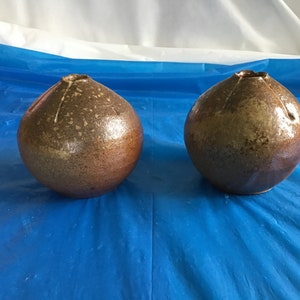 May include: Two brown ceramic vases with a speckled glaze. The vases are round and have a wide opening at the top.