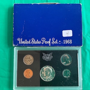 May include: A 1968 United States Proof Set in a blue box. The set includes various coins, such as a nickel, penny, quarter, and half dollar, displayed in a clear plastic case. The box is labeled "United States Proof Set 1968".