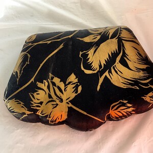 May include: A black velvet cushion with a gold floral pattern. The cushion is shaped like a heart and has a quilted texture.