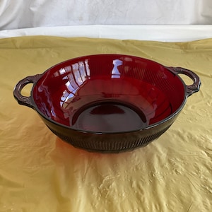 May include: A deep red glass bowl with two handles. The bowl has a ribbed design and is perfect for serving salads, fruit, or snacks.
