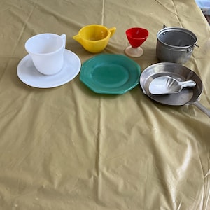 May include: A set of miniature kitchenware, including a white teacup and saucer, a yellow creamer, a red cup, a green plate, a silver pan with a white scoop, and a silver pot with a handle.