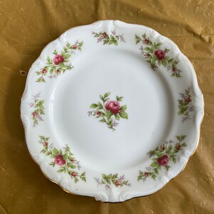 May include: A white porcelain plate with a gold rim and a floral design featuring pink roses and green leaves.