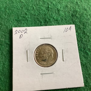 May include: A close-up of a 2002-D United States dime coin on a white background. The coin is in good condition and has a gold color. The coin is labeled with the year 2002 and the mint mark D. The coin is also labeled with 10¢.