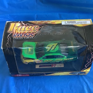 May include: A green and yellow die-cast model car with the number 97 and the words "John Deere" on the side. The car is in a clear plastic display case with a black base. The case is labeled "Race Image Collectibles" and "Dimension 4".