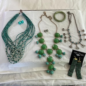 May include: An assortment of jewelry including necklaces, earrings, and a bracelet. The necklaces feature green and turquoise beads and stones. One necklace has a multi-strand design. Earrings are also green and turquoise.