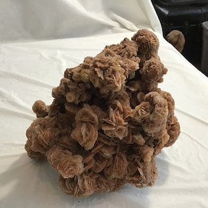 May include: A large, brown, rose quartz geode with a rough, textured surface. The geode is made up of many small, rose-shaped crystals.
