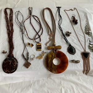 May include: A collection of necklaces and earrings with various pendants, including a large round pendant with a brown and orange swirl pattern, a smaller round pendant with a black and white pattern, and a triangular pendant with a black stone. The necklaces are made of different materials, including beads, leather, and metal.