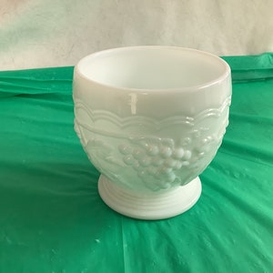 May include: A white milk glass bowl with a grapevine design. The bowl has a pedestal base and is perfect for serving fruit or snacks.