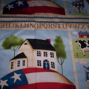 May include: A colorful fabric with a red, white, and blue American flag design. The fabric features a house with a white exterior and a red roof, a cow, and a mailbox with a birdhouse on top. The fabric also includes the letters of the alphabet, "DEFGHIJKLMNOPQRSTUVWXYZ".