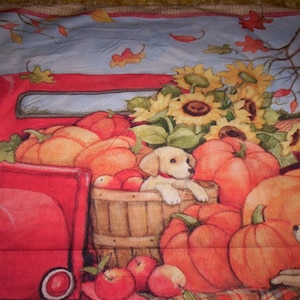 May include: A red pickup truck filled with pumpkins and sunflowers. Two golden retriever puppies are sitting in the bed of the truck, one with a basket of apples.
