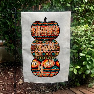 Könnte beinhalten: Eine Gartenflagge aus Burlap mit einem Stapel von drei Kürbissen. Die Kürbisse sind mit einem bunten geometrischen Muster verziert und die Worte "Happy Fall Y'all" sind in goldenen Glitzer geschrieben.