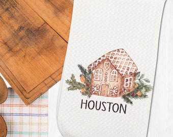 May include: White kitchen towel featuring an illustration of a gingerbread house with icing and candy decorations. The text "HOUSTON" is printed below the house.