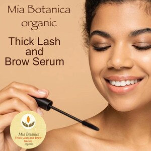 K&ouml;nnte beinhalten: Eine Frau tr&auml;gt einen schwarzen Mascara-Applikator auf ihre Wimpern auf. Die Produktverpackung ist unten links sichtbar und tr&auml;gt den Schriftzug "Mia Botanica Thick Lash and Brow Serum organic".