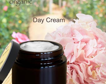 May include: A brown glass jar with a white cream inside. The jar has a black lid and the text "Mía Botánica organic Day Cream" is printed on the label.