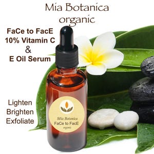 May include: A brown glass bottle with a dropper top, labeled "Mia Botanica Face to Face organic" and "10% Vitamin C & E Oil Serum". The bottle is sitting on a green leaf with white stones and a white flower.