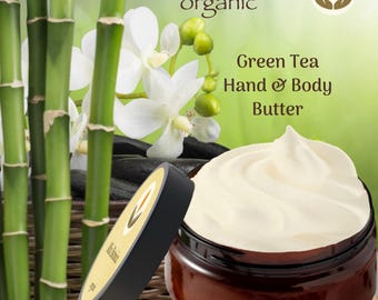 May include: A jar of Green Tea Hand & Body Butter with a black lid, next to a bamboo stalk and white orchid flowers. The jar is open, revealing a swirl of creamy white butter. The label reads "Mía Botánica organic."