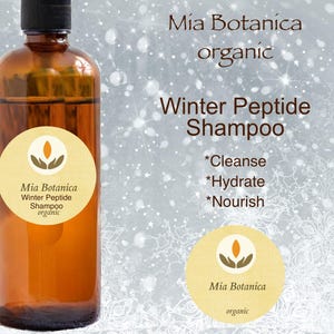 May include: A brown glass bottle with a label that reads "Mia Botanica Winter Peptide Shampoo organic". The bottle is on a silver background with a snowflake pattern.