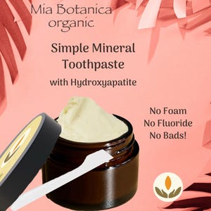 May include: A jar of Simple Mineral Toothpaste with Hydroxyapatite, with a white scoop. The jar is dark brown with a black lid. The text on the image says "Mía Botanica organic" and "No Foam, No Fluoride, No Bads!"