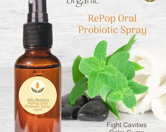 Op de afbeelding: Een bruine glazen fles RePop Oral Probiotic Spray met een zwarte sproeikop. Het etiket luidt "Mia Botanica organic". Verse muntbladeren en zwarte stenen zijn naast de fles geplaatst. Tekst op de afbeelding luidt "Fight Cavities, Calm Gums, Freshen Breath."