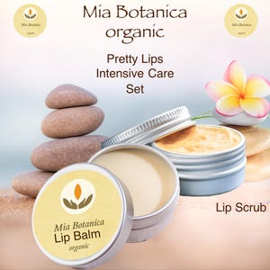 May include: A set of two organic lip care products in silver tins. The lip balm tin has a yellow label with the text "Mia Botanica Lip Balm organic". The lip scrub tin has a white label with the text "Lip Scrub".