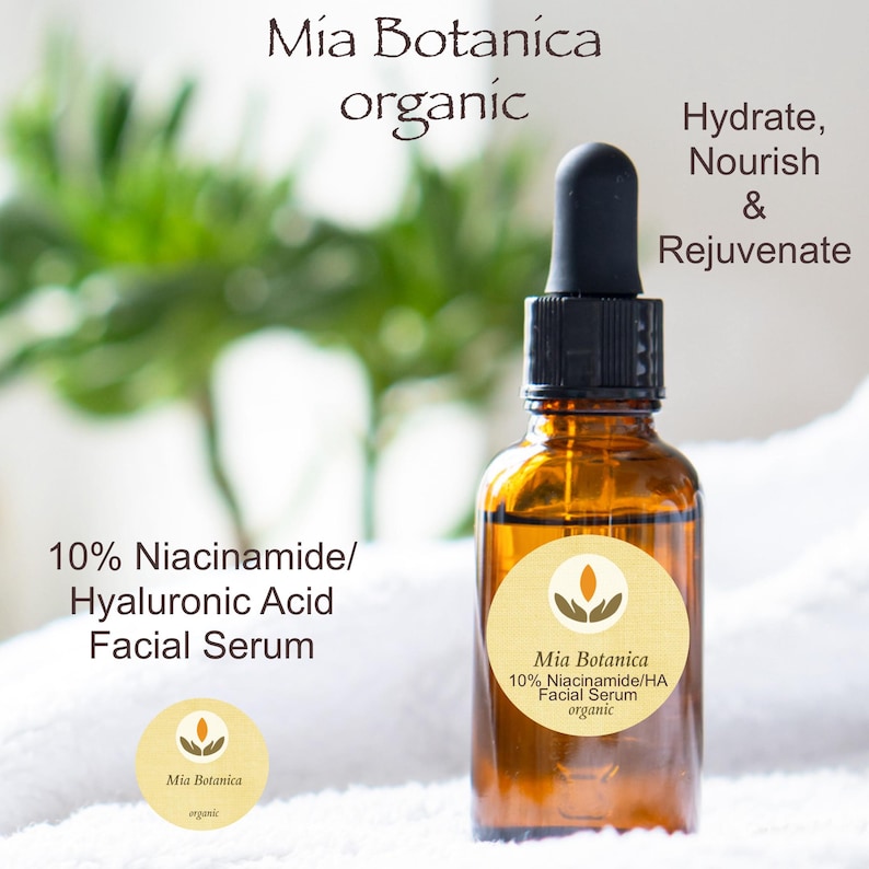 May include: A glass bottle of organic facial serum with a dropper. The bottle is labelled "Mia Botanica 10% Niacinamide/HA Facial Serum organic". The bottle is sitting on a white surface with green foliage in the background. The text "Hydrate, Nourish & Rejuvenate" is written in black above the bottle.