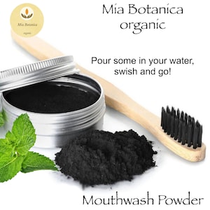 May include: A small silver container with a black powder inside. The container is labeled "Mia Botanica organic Mouthwash Powder". There is a wooden toothbrush with black bristles and a sprig of green mint leaves next to the container.