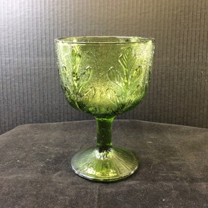 Puede incluir: Una copa de vidrio verde con un diseño de hojas. La copa tiene una copa ancha y un tallo alto.