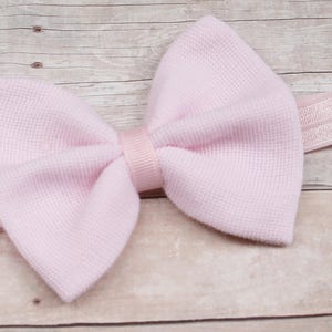 以下が含まれることがあります： ピンクの布製のボウヘアバンドとゴムバンド