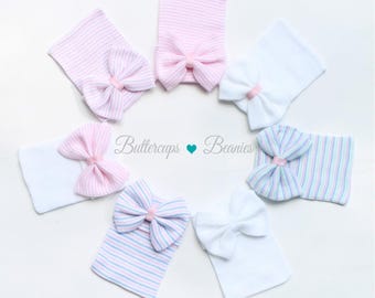 May include: Six newborn baby hats with bows. The hats are in pink, white, and blue stripes. The bows are pink.