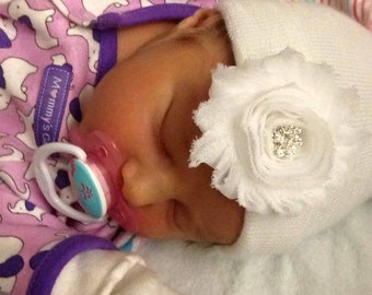 May include: A newborn baby wearing a white hat with a white flower and a rhinestone center. The baby is wearing a purple and pink onesie with a white elephant print. The onesie has the text "Mommy's Girl" on the side. The baby is sleeping peacefully.