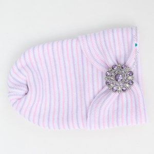 May include: A pink and purple striped baby hat with a large silver and purple rhinestone button.