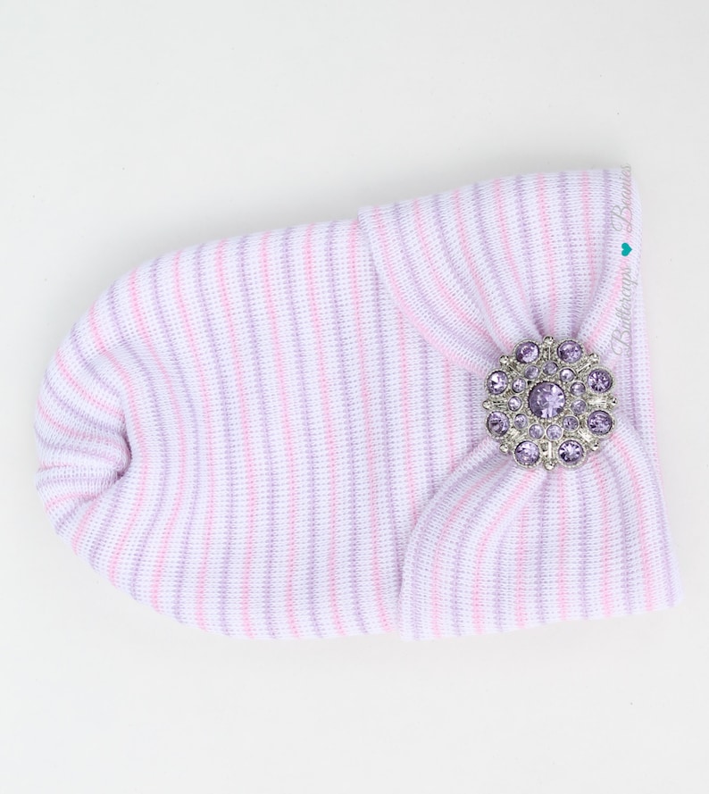 May include: A pink and purple striped baby hat with a large silver and purple rhinestone button.
