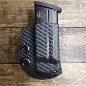May include: Black carbon fiber magazine holster with two screws. The holster is designed to hold a magazine for a handgun.