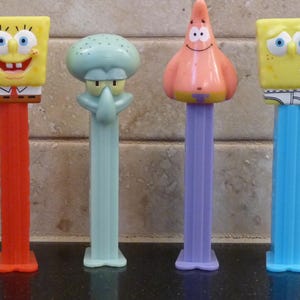 May include: Four PEZ dispensers featuring characters from the animated series SpongeBob SquarePants. The dispensers include SpongeBob, Squidward, and Patrick. The dispensers have colorful plastic stems and character heads. The SpongeBob dispensers are yellow, Squidward is light blue, and Patrick is pink.