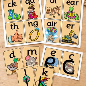 May include: A collection of educational phonics cards featuring letters and digraphs paired with colourful illustrations. The cards display text such as ck, qu, oi, ear, th, ng, air, er, d, m, e, c, l, and k, alongside images of a sock, queen, bunnies, alien, thumb, ring, chair, excavator, duck, mouse, elephant, cat, lollipop, and kite.
