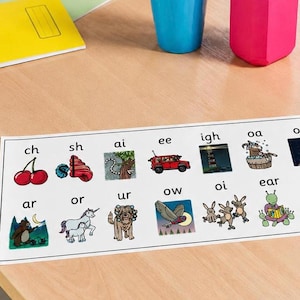 May include: A rectangular educational phonics chart printed on white paper featuring two rows of letter combinations paired with colorful illustrations including cherries, a shell, a car, a lighthouse, a goat, a bear, a unicorn, a dog, an owl, and rabbits.